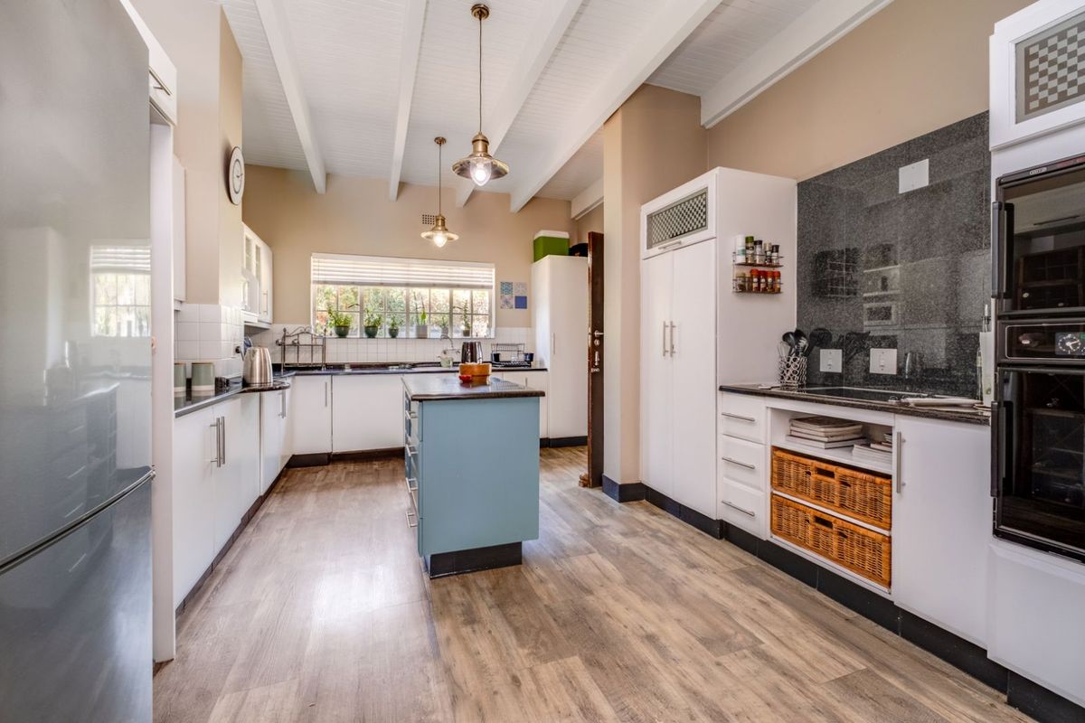 A well-appointed kitchen featuring white cabinetry, a central island, granite countertops, a built-in oven, and exposed beam ceilings.