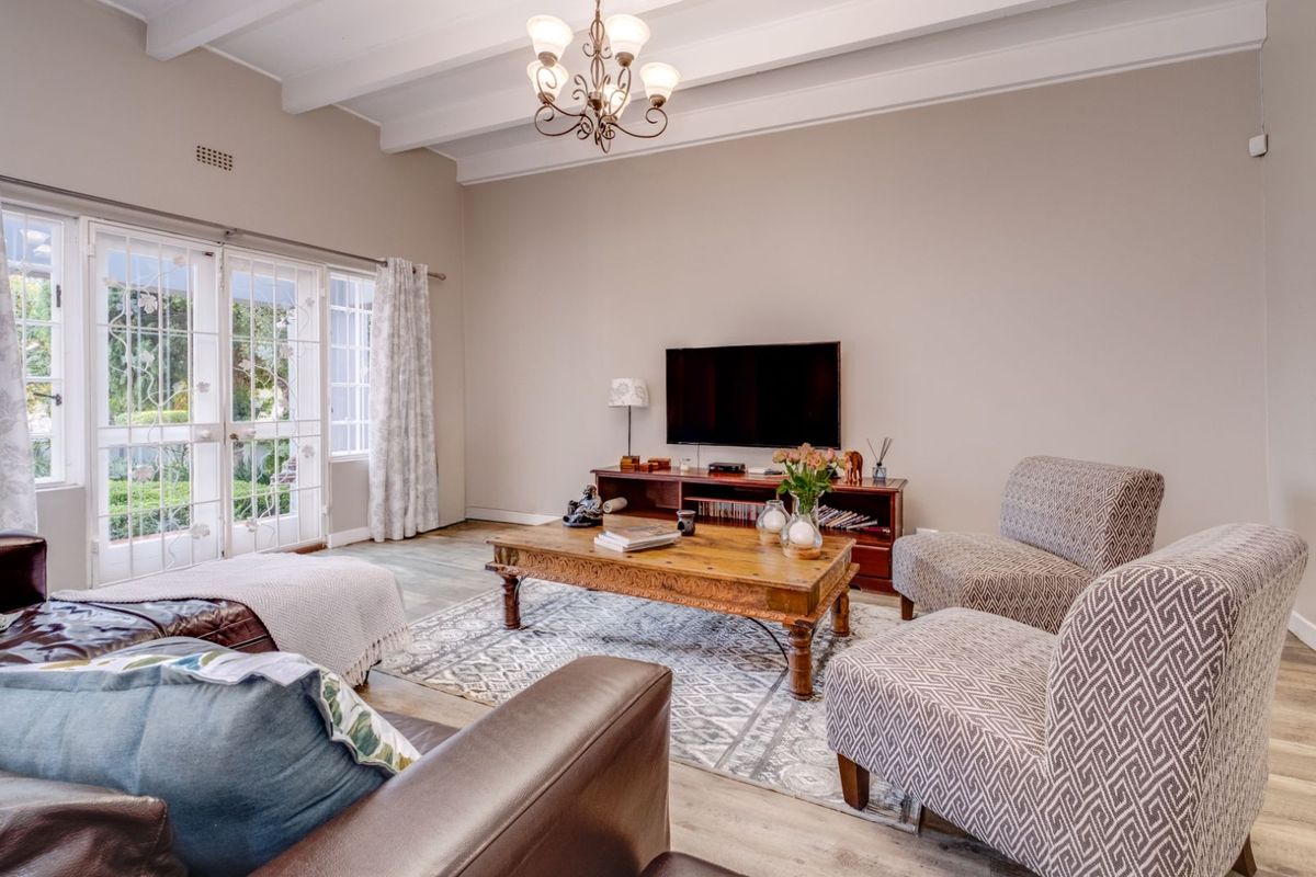 Spacious living room featuring exposed beam ceilings, wood-look flooring, and large glass panel doors providing direct access to the outdoor area.