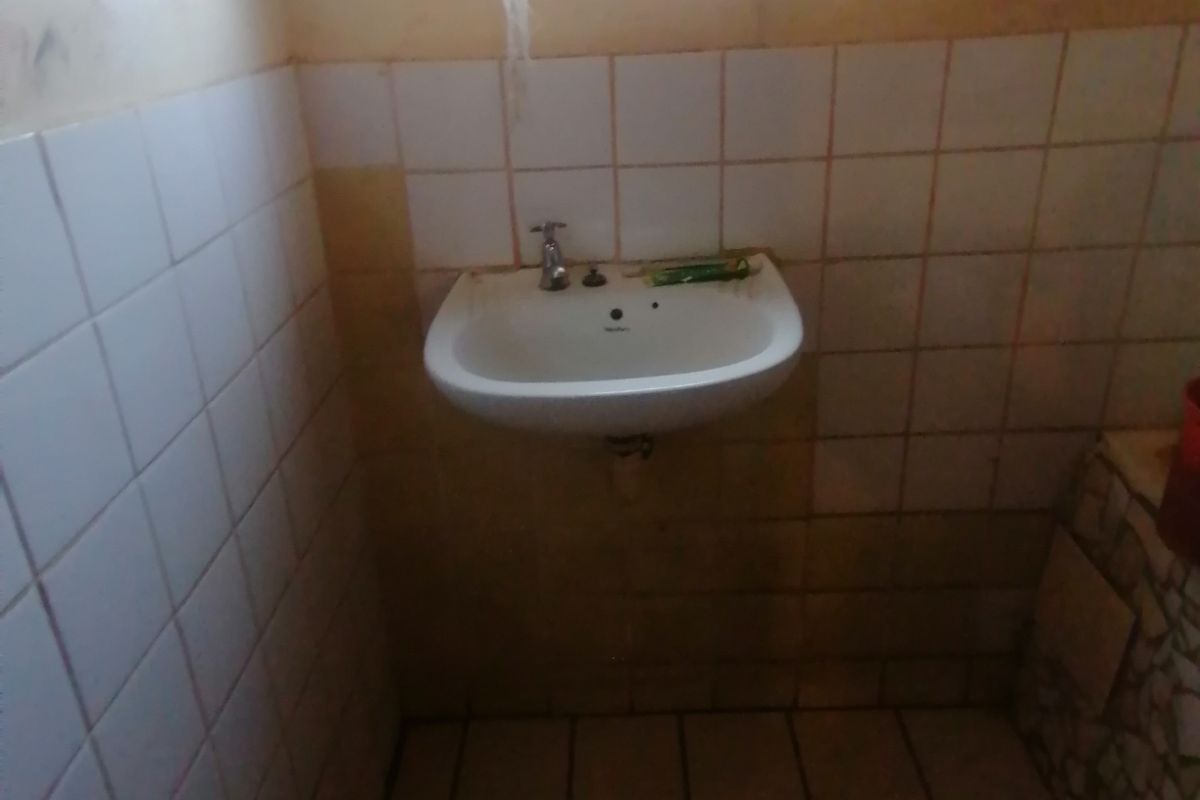 A small bathroom featuring a wall-mounted basin, tiled walls, and floor tiles, requiring cosmetic updates and maintenance.