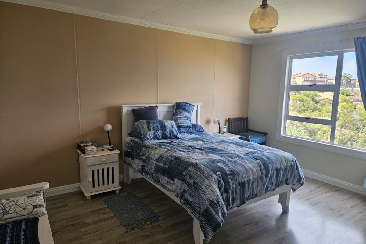 A well-lit bedroom featuring wood-look laminate flooring, neutral wall finishes, and a large window offering an elevated view of the surrounding landscape.