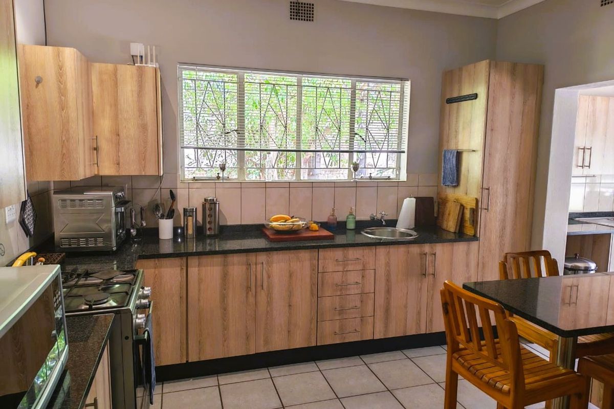 A functional kitchen featuring light wood-grain cabinetry, dark granite countertops, tiled flooring, and a large window providing natural light.