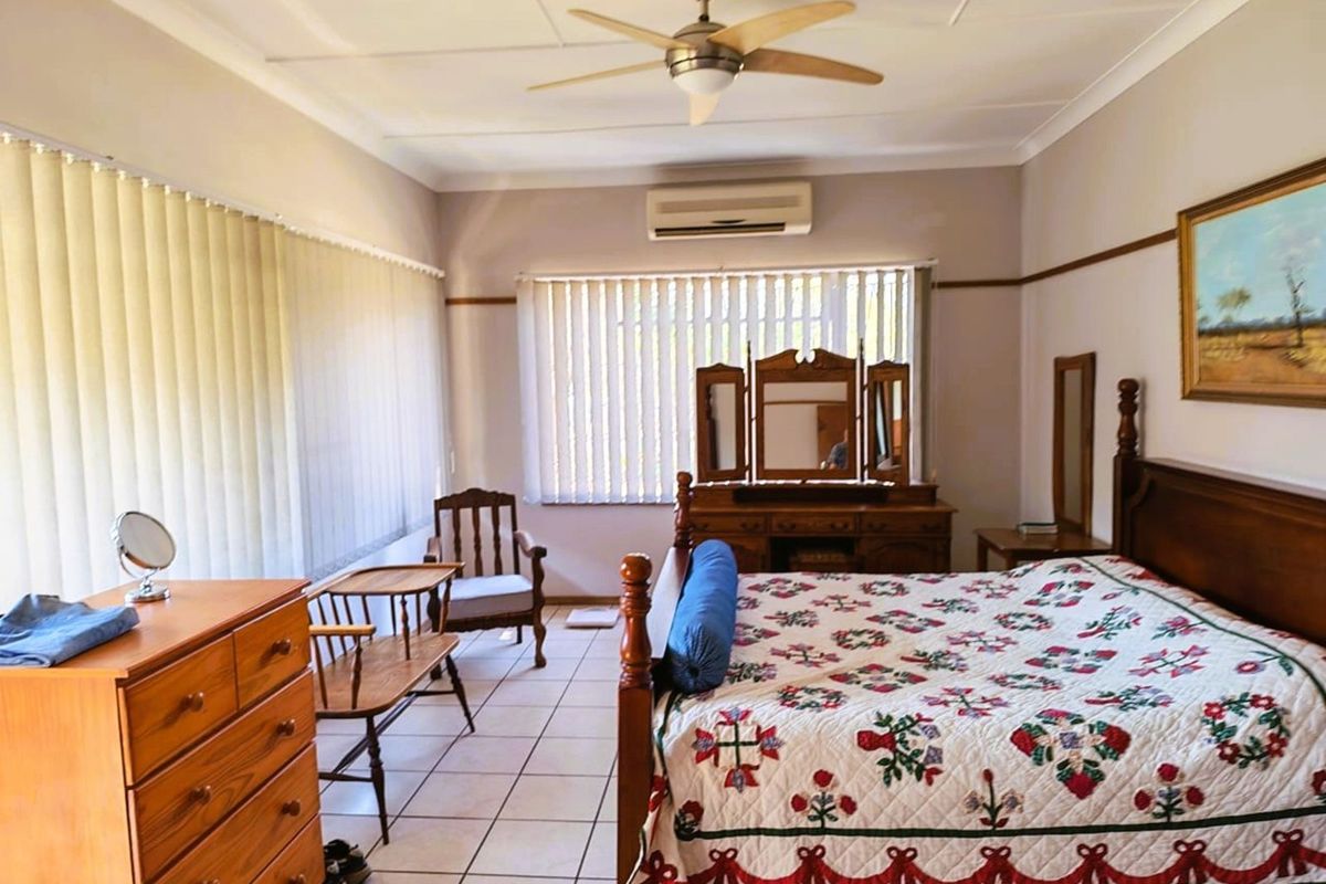 Spacious bedroom featuring tiled flooring, a ceiling fan, and a wall-mounted air conditioning unit, offering a functional and comfortable living space.