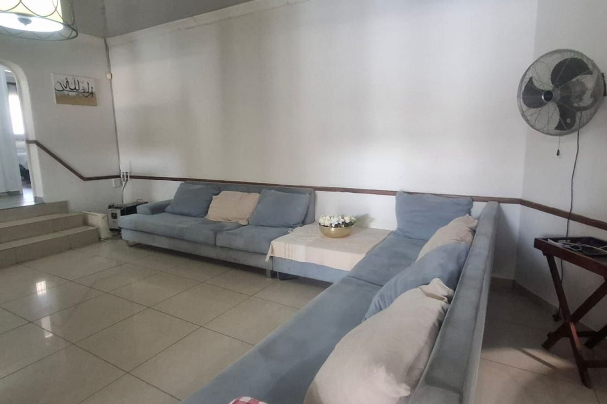 Spacious living room featuring tiled flooring, a raised step leading to an adjacent area, and a wall-mounted fan.