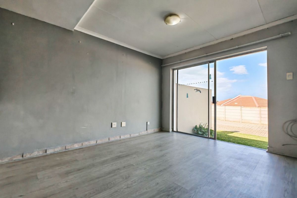 An empty living room featuring grey laminate flooring, neutral walls, and a large sliding glass door providing direct access to the rear garden area.