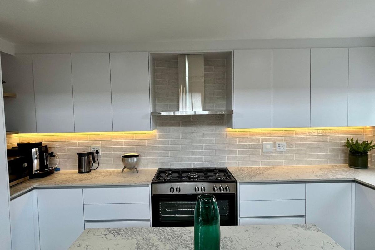 Modern kitchen featuring sleek white cabinetry, stone countertops, a gas range with stainless steel extractor hood, and stylish subway tile backsplash with under-cabinet lighting.