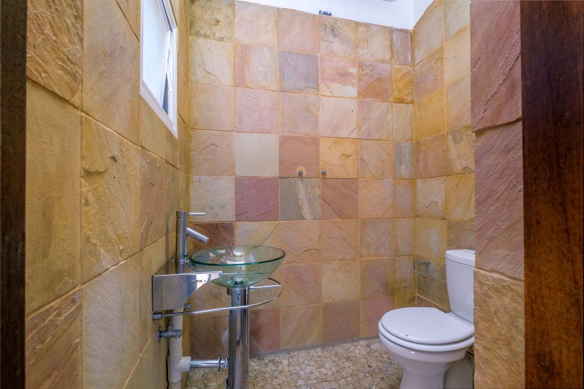 Compact bathroom featuring natural stone wall tiling, a glass vessel sink with pedestal, and a standard toilet.