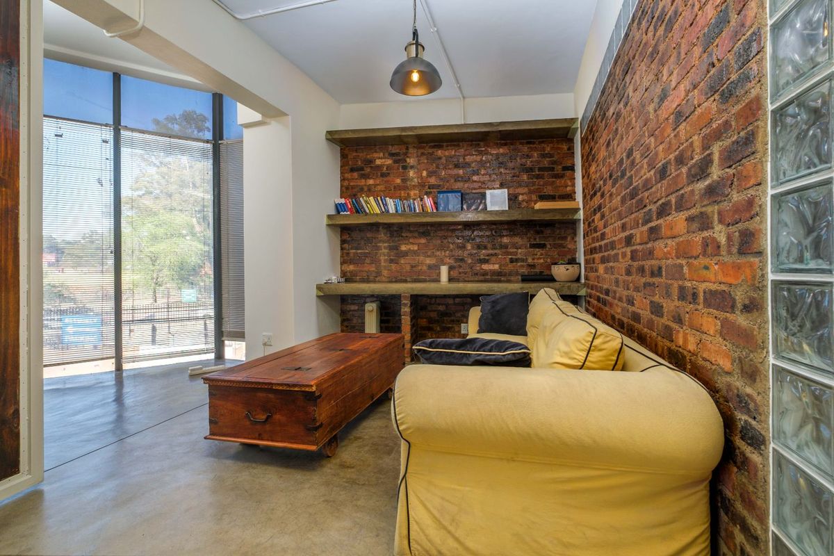 A modern industrial-style living area featuring exposed brick walls, polished concrete floors, floor-to-ceiling windows, and built-in timber shelving.