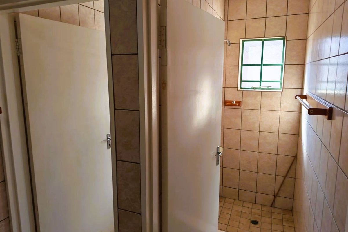 A functional bathroom space featuring tiled walls and flooring, a walk-in shower area, and a small window for natural light.