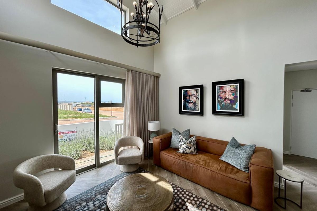 Bright living room featuring high vaulted ceilings, large windows, and sliding glass doors leading to an outdoor area with herringbone flooring.