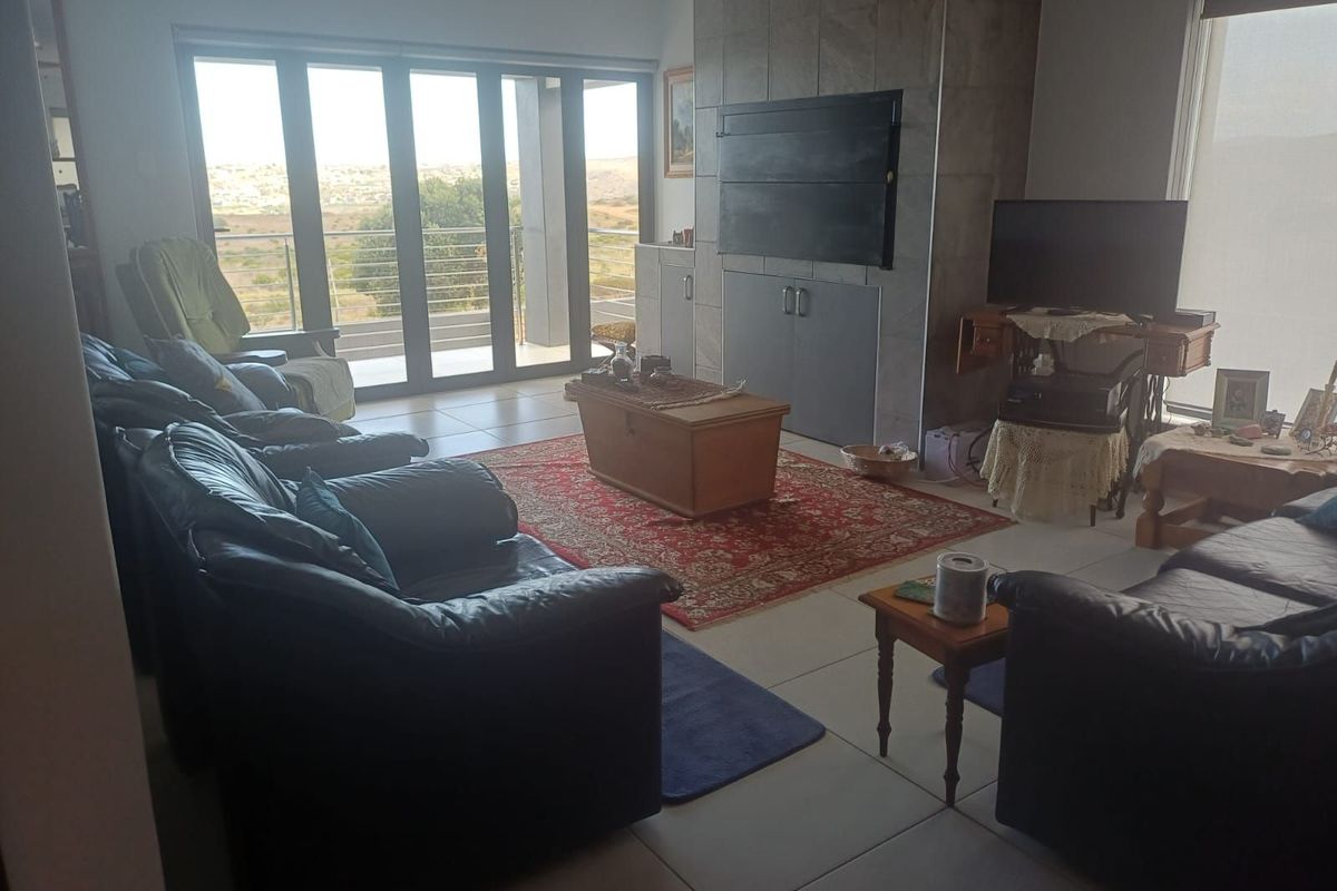 Spacious living room featuring a large stone-clad fireplace, tiled flooring, and expansive sliding glass doors leading to an outdoor balcony with scenic views.