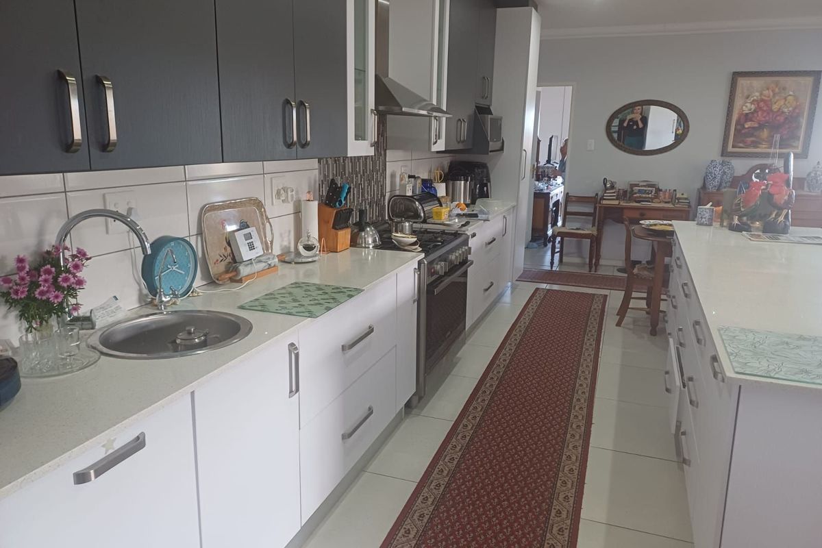 Modern kitchen featuring two-tone cabinetry, stone countertops, a stainless steel gas stove with extractor fan, and a central island with breakfast bar seating.