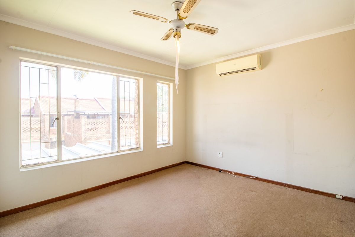 A vacant bedroom featuring neutral walls, carpeted flooring, a ceiling fan, and a wall-mounted air conditioning unit with large windows.