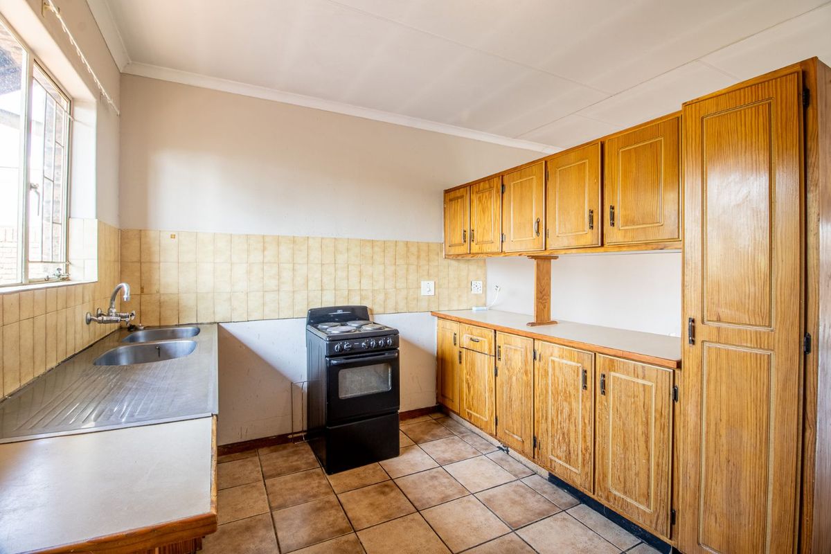 A functional kitchen featuring wooden cabinetry, a double stainless steel sink, tiled flooring, and a freestanding stove with a tiled backsplash.