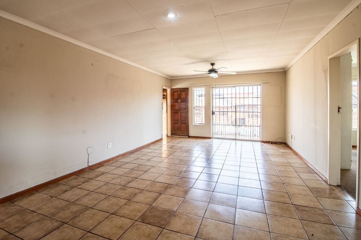 An empty, open-plan living area featuring tiled flooring, a ceiling fan, and direct access to an exterior entrance with security gates.