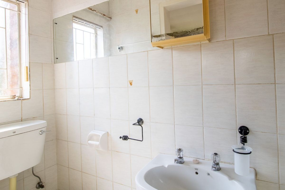A dated bathroom featuring white wall tiles, a pedestal basin, and a wall-mounted mirror cabinet, requiring cosmetic updates and maintenance.