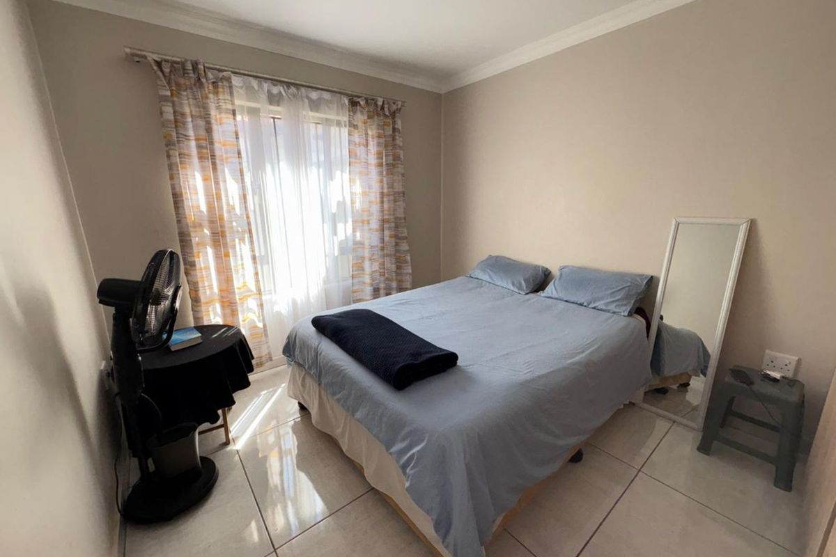 A well-lit bedroom featuring neutral wall tones, large format floor tiles, and a window with curtain tracks.