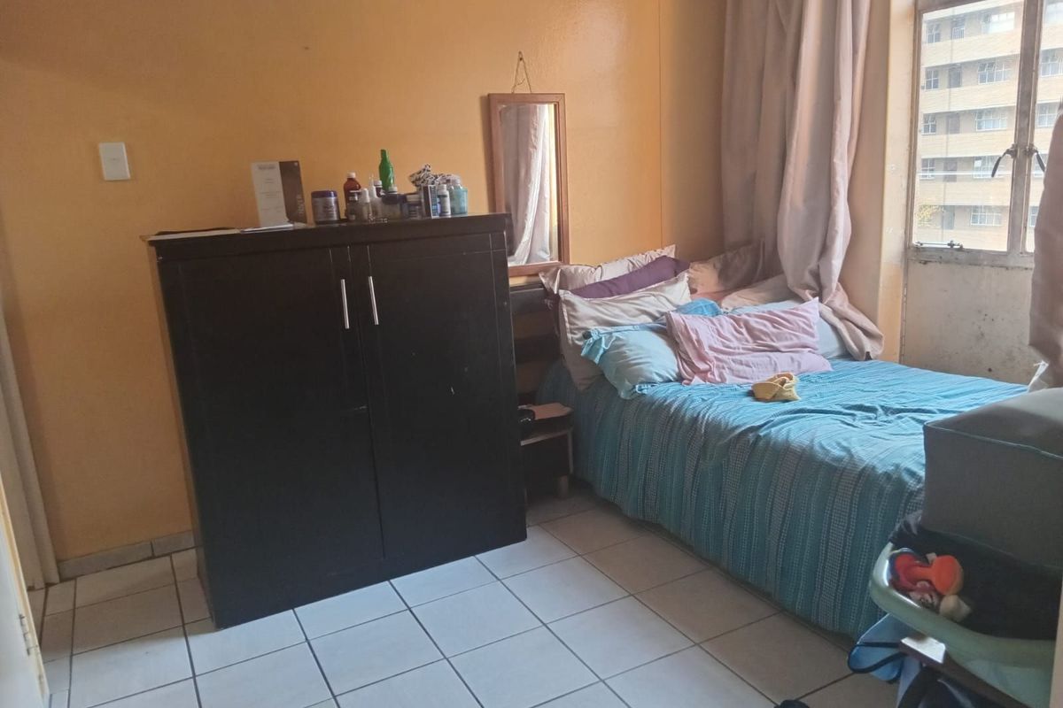 A bedroom featuring tiled flooring and a large window with natural light, providing a functional space for rest.