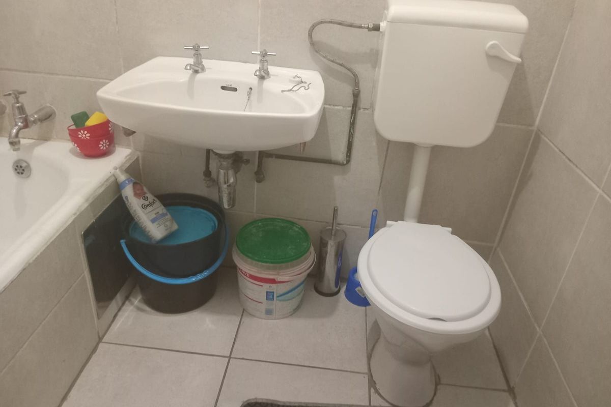 A compact bathroom featuring a wall-mounted basin, a standard toilet, and tiled walls and flooring, requiring some maintenance and cosmetic updates.