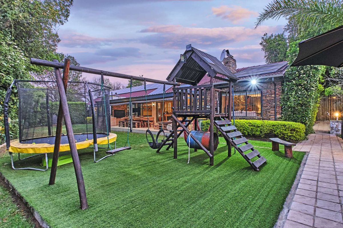 Rear garden area featuring artificial lawn, a children's play structure, and a paved walkway leading to the main house with stone cladding.