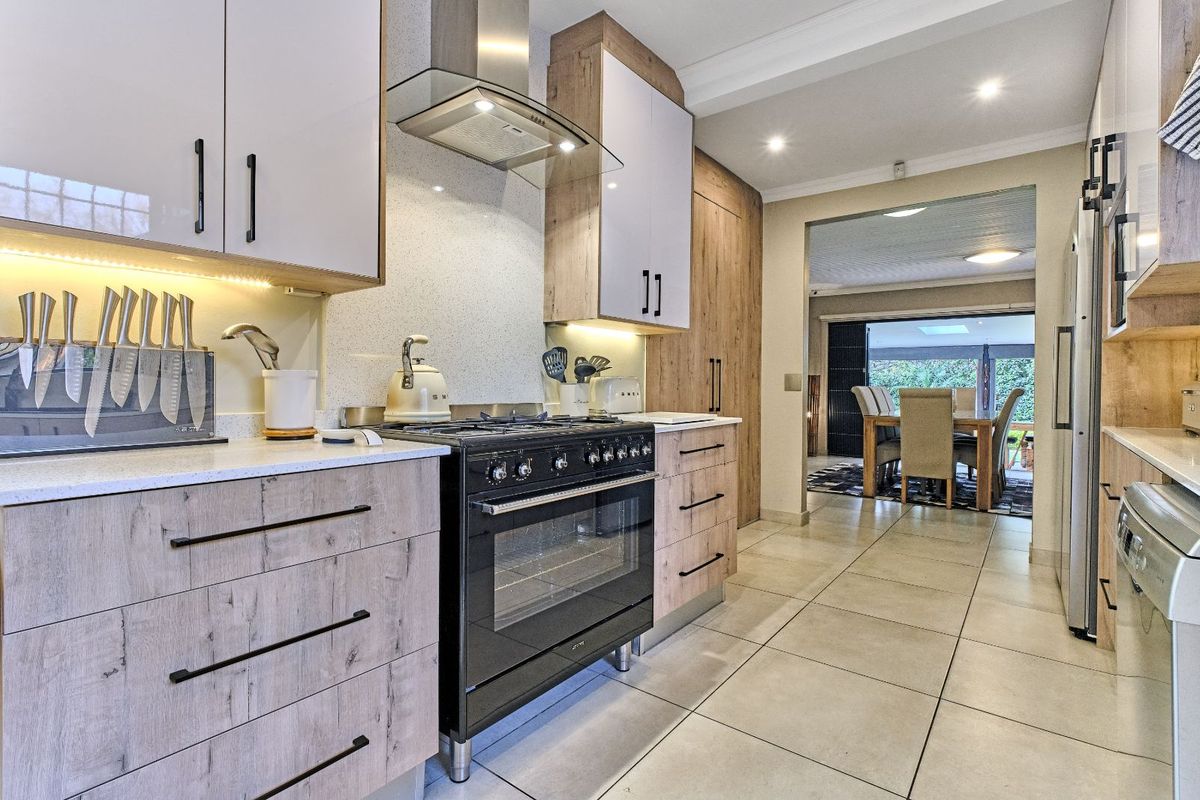 Modern kitchen featuring wood-grain and white cabinetry, stone countertops, a stainless steel extractor fan, and a large black gas range cooker.