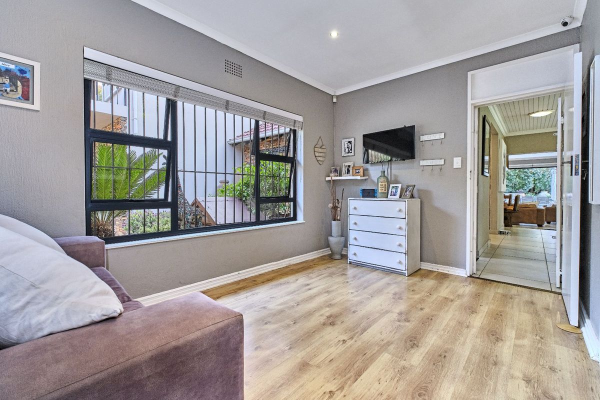 A living room featuring light wood-look flooring, grey walls, and a large window with security bars, providing a view of the exterior.