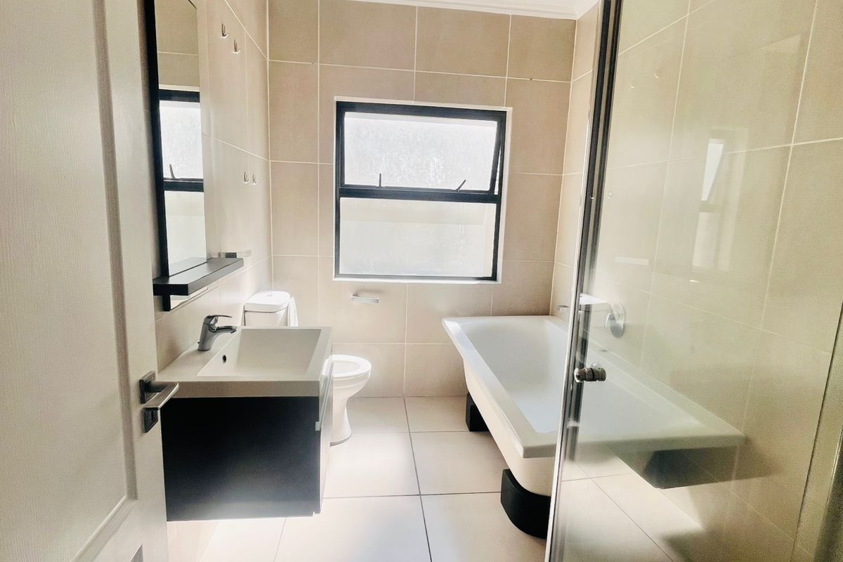 Modern bathroom featuring a wall-mounted vanity, a separate bathtub, and a glass-enclosed shower with neutral floor-to-ceiling tiling.
