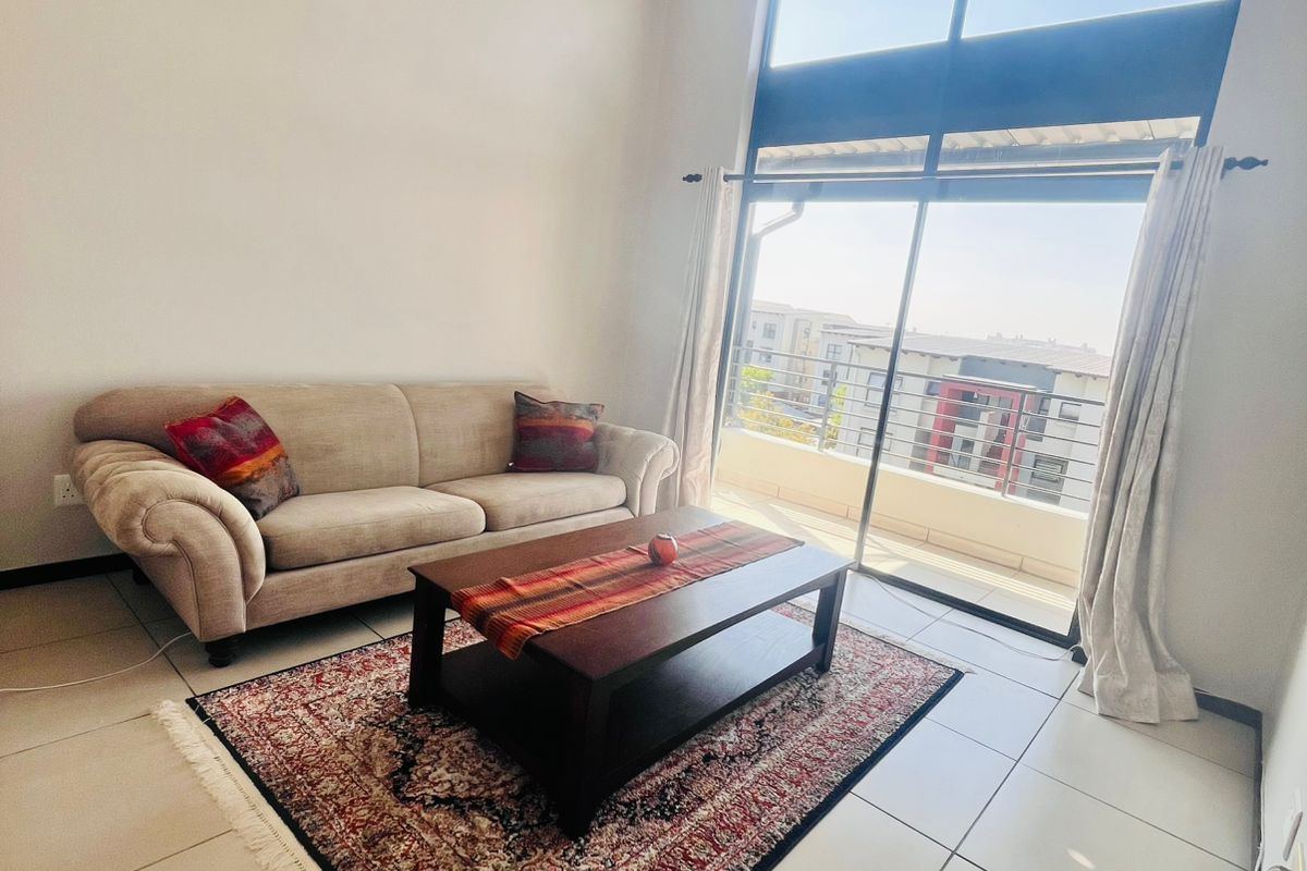 Bright living area featuring high ceilings, large windows, and sliding glass doors leading to a private balcony with an urban view.