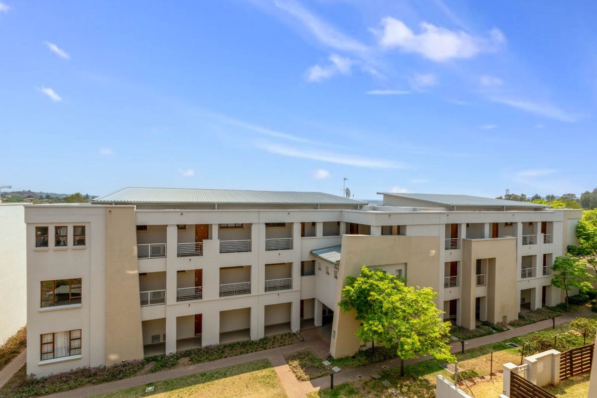 An elevated view of a modern apartment complex featuring multi-level balconies, paved walkways, and landscaped garden areas.