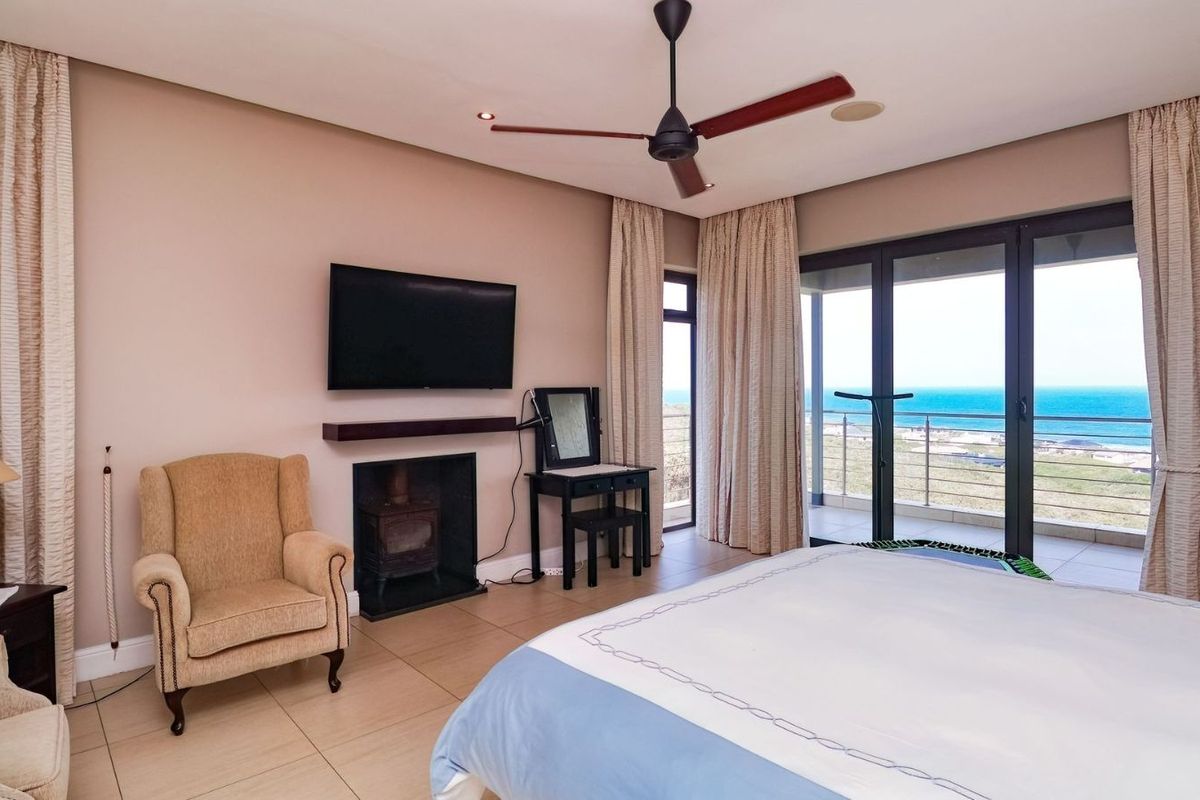 Spacious bedroom featuring tiled flooring, a built-in fireplace, ceiling fan, and large sliding doors opening to a balcony with ocean views.