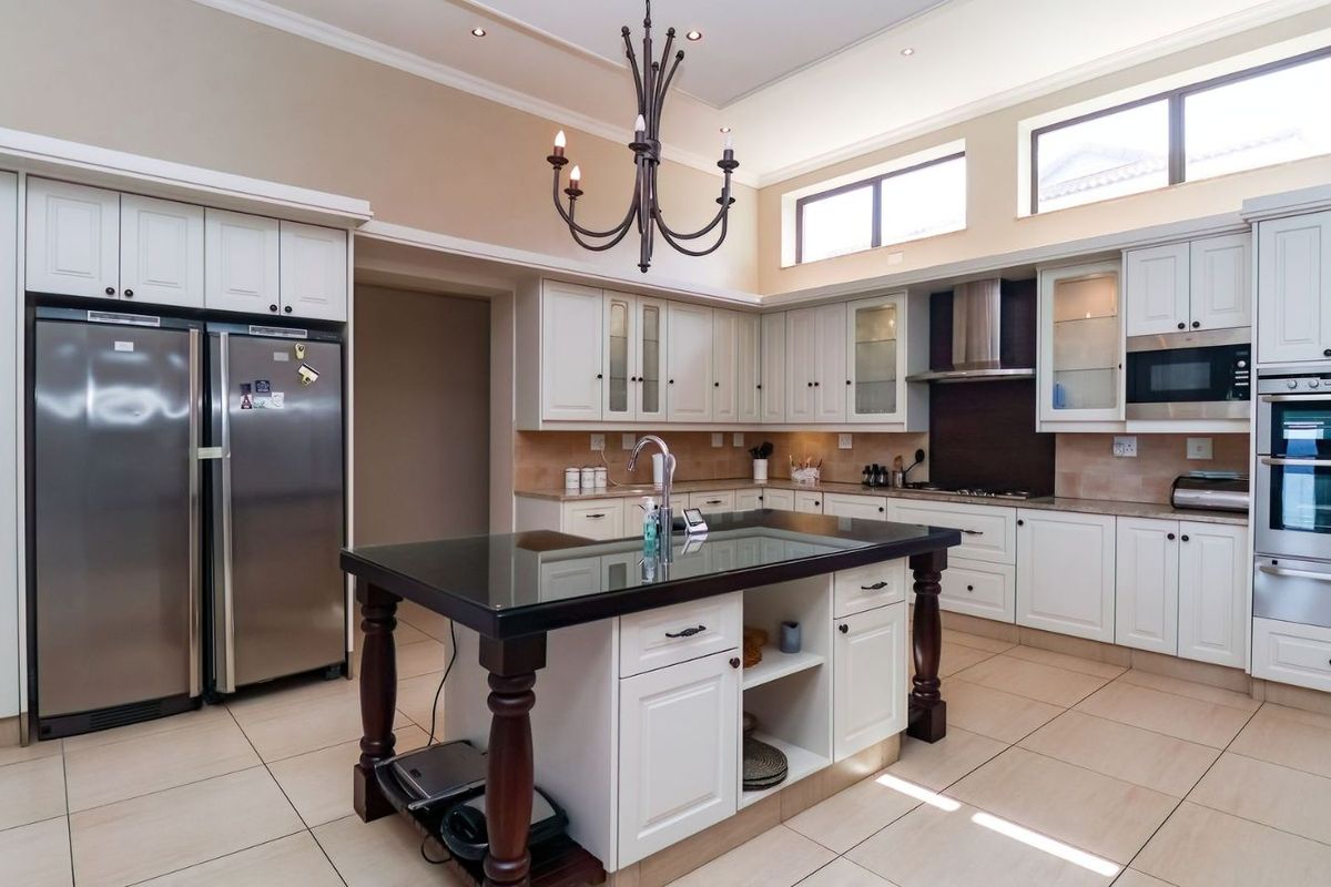 Spacious kitchen featuring white cabinetry, a central island with a dark countertop, built-in oven, microwave, and high-level windows providing natural light.