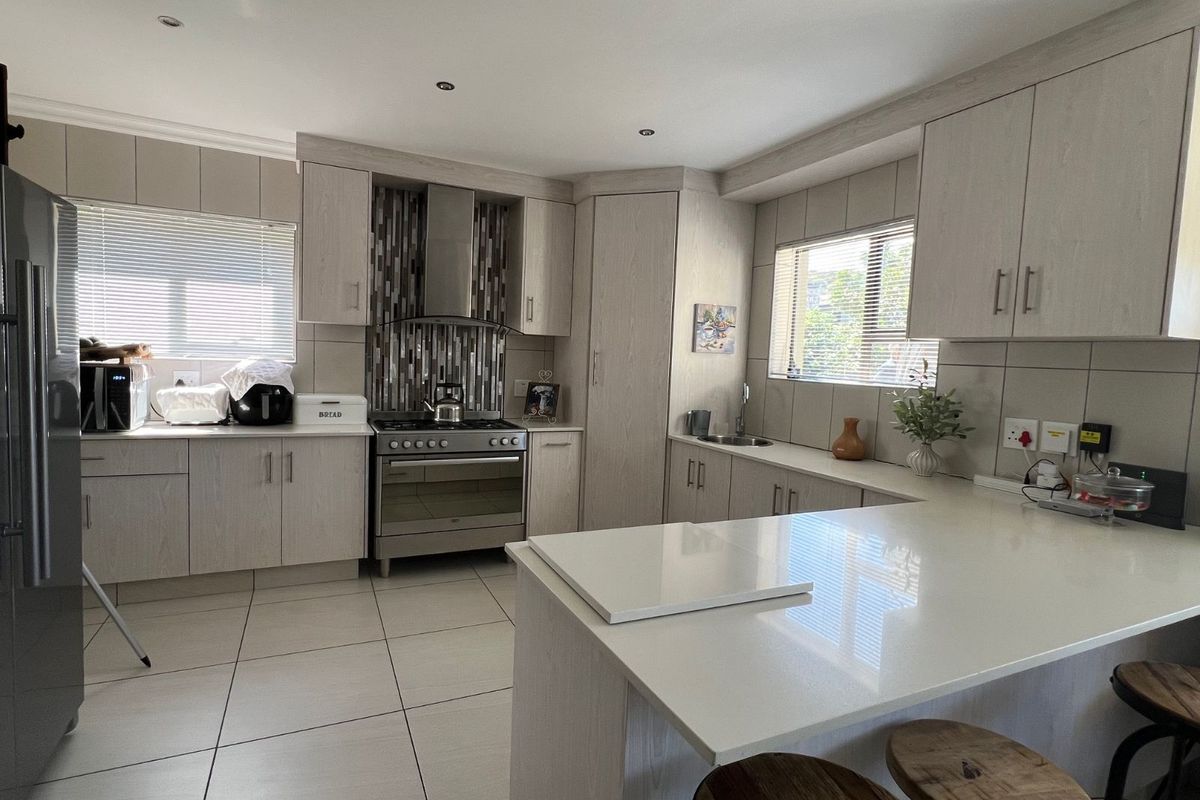 Modern kitchen featuring light wood-grain cabinetry, stone countertops, a stainless steel gas stove with extractor fan, and tiled flooring.