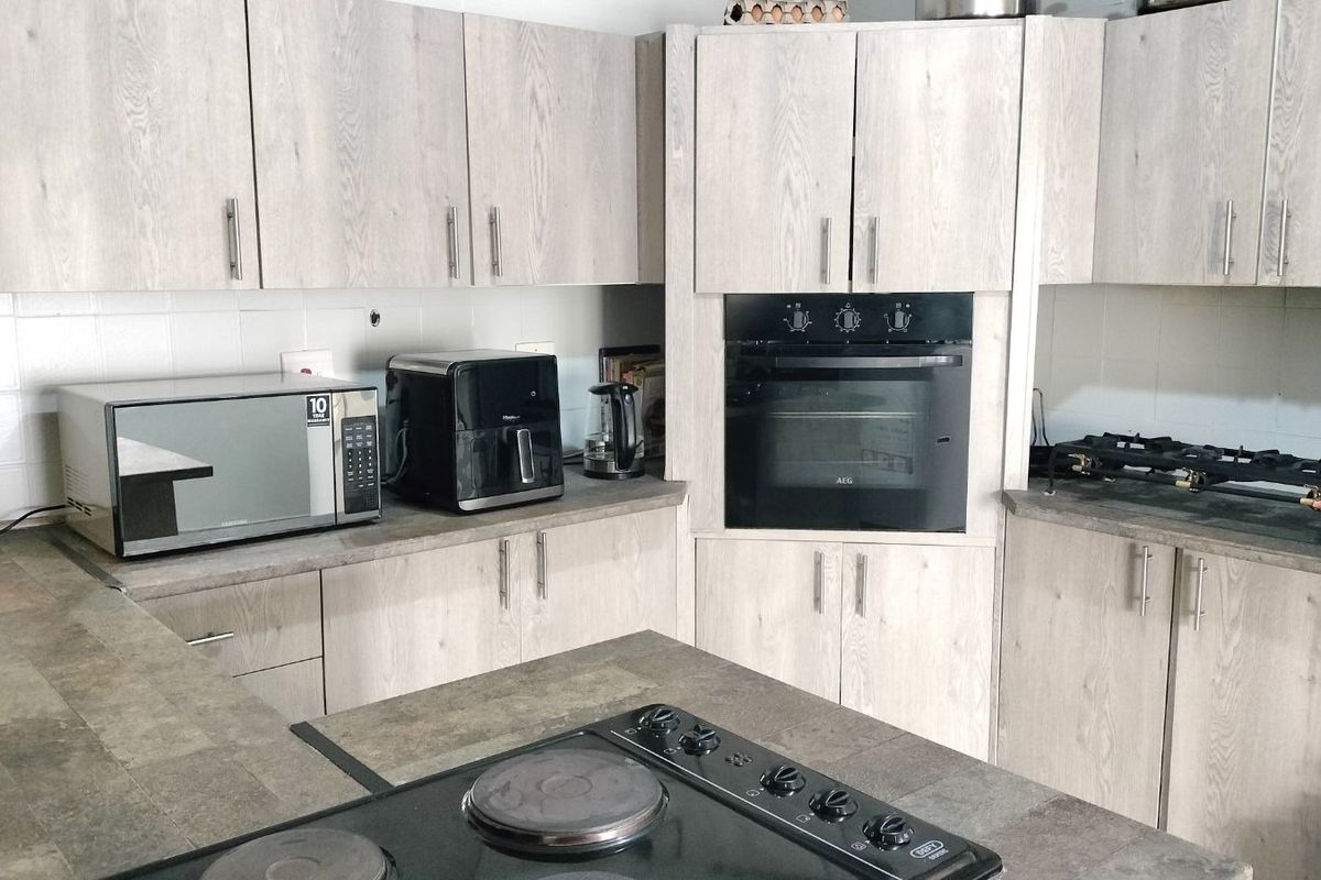 A functional kitchen featuring light wood-grain cabinetry, stone-look countertops, a built-in oven, and a separate electric hob on the kitchen island.