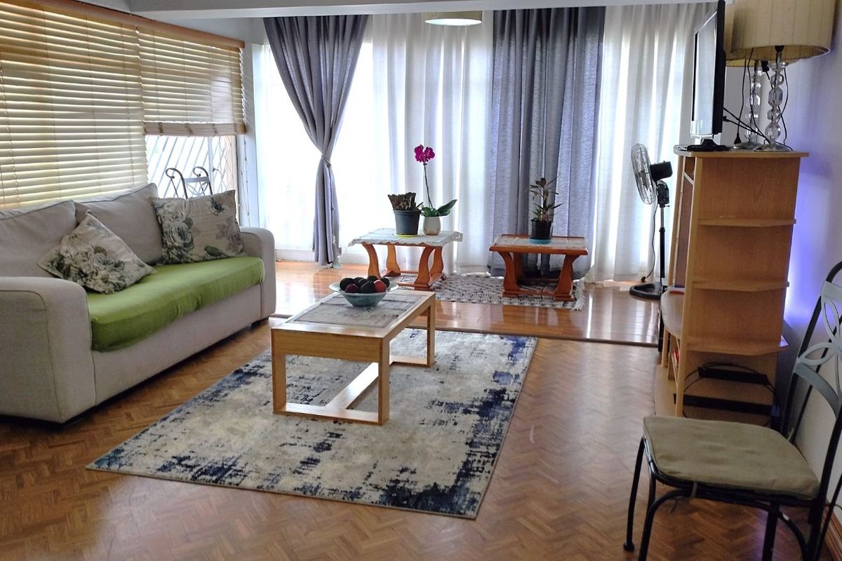 A comfortable living room featuring parquet flooring, large windows with blinds and curtains, and a bright, open layout.