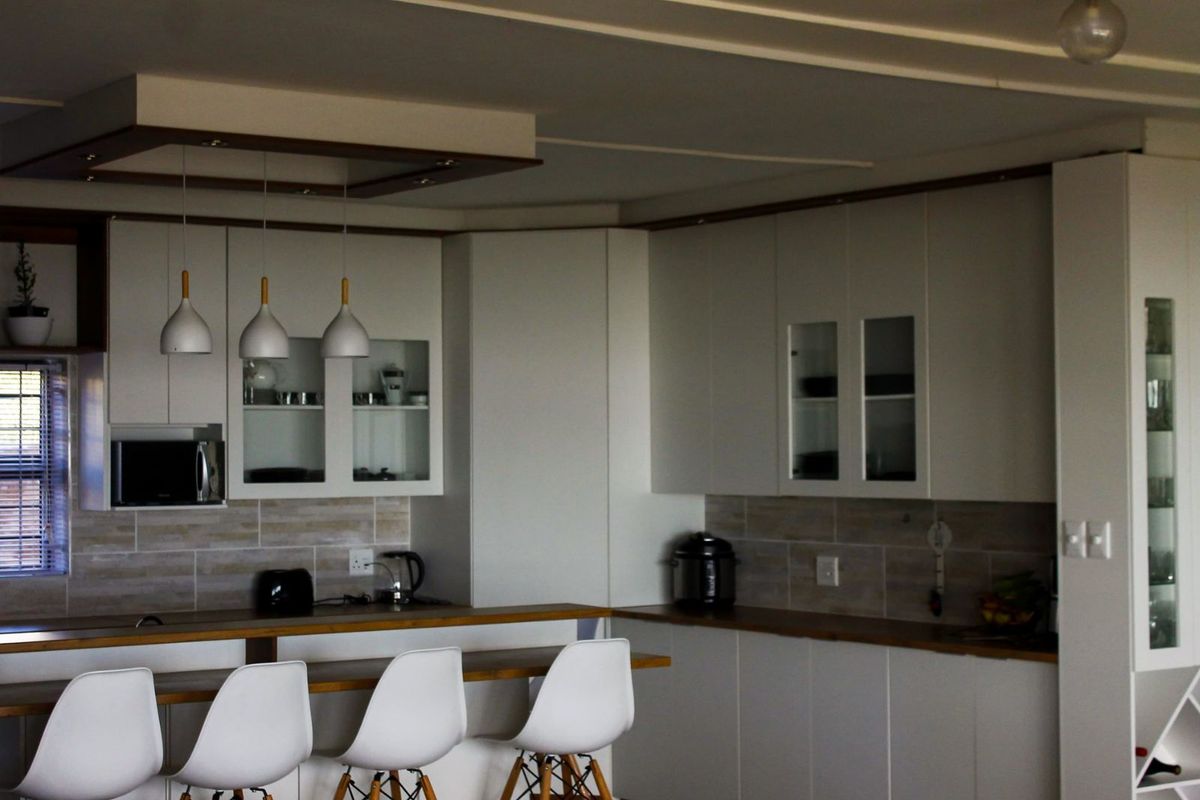 Modern kitchen featuring white cabinetry, wooden countertops, a breakfast bar, and integrated lighting, creating a clean and functional culinary space.