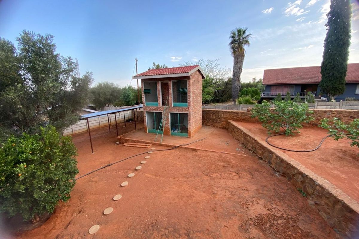 A spacious backyard featuring a two-story brick utility structure, stone retaining walls, and a covered side walkway area.