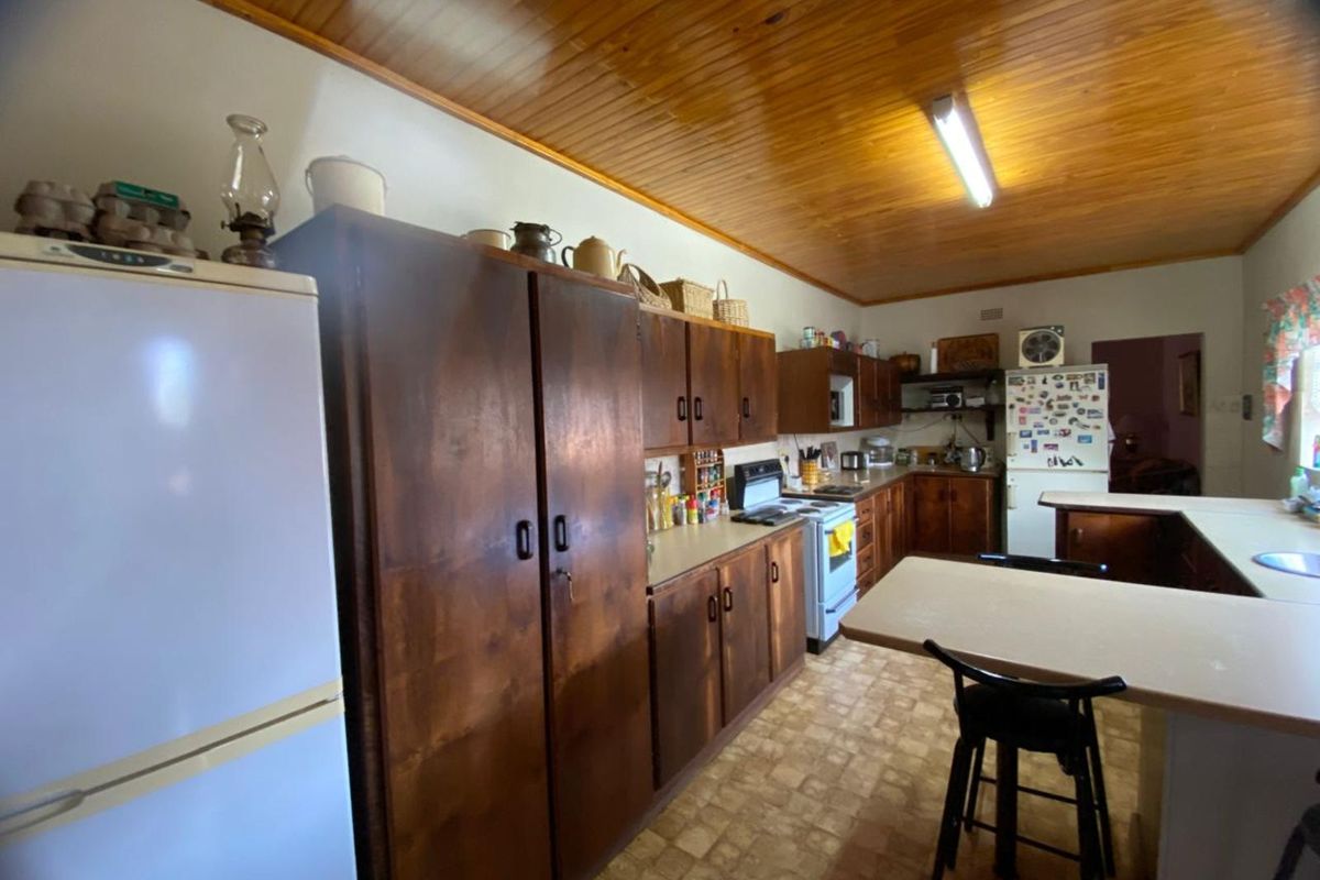 A dated kitchen featuring wooden cabinetry, a timber-paneled ceiling, and a breakfast bar, offering significant potential for a modern renovation.