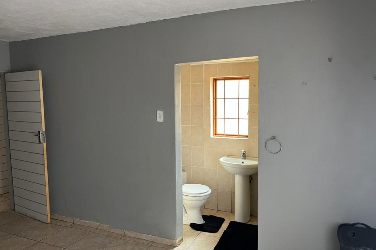A functional bathroom featuring a pedestal basin, toilet, and tiled flooring, accessible from the adjacent living area.