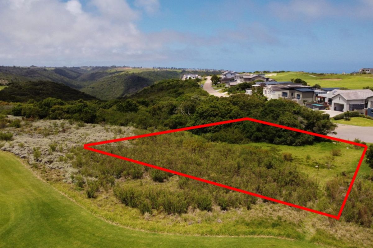 An aerial view of a vacant residential plot highlighted in red, situated within a scenic estate with surrounding natural vegetation and nearby residential properties.