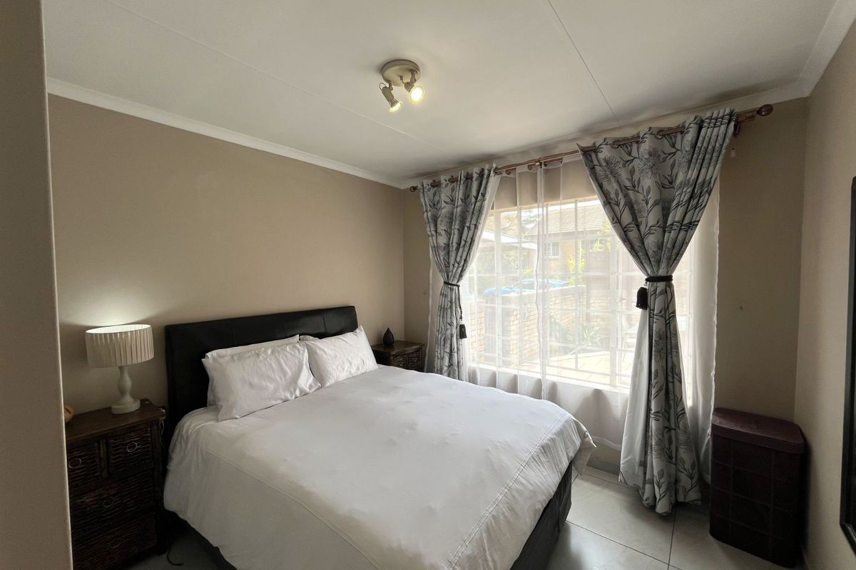 A well-lit bedroom featuring tiled flooring, neutral wall finishes, and a large window with security bars, providing natural light and a view of the exterior.