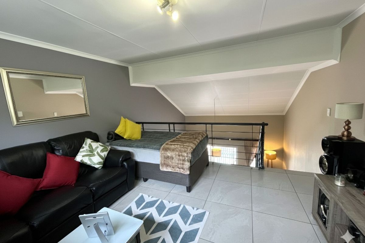 A mezzanine level living area featuring tiled flooring, a metal balustrade overlooking the lower level, and a vaulted ceiling.
