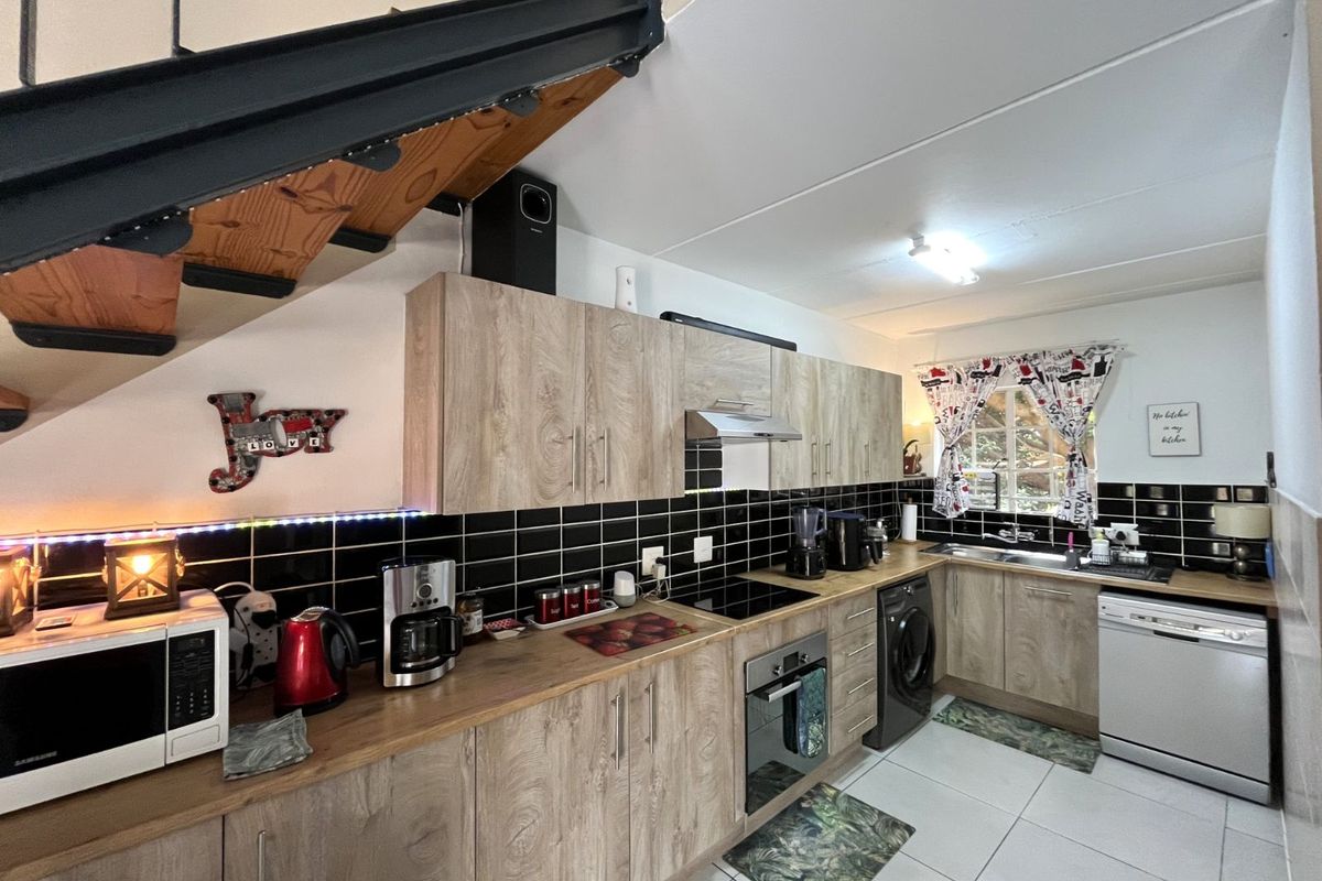 A functional kitchen featuring wood-look cabinetry, black subway tile backsplash, built-in oven, hob, extractor fan, and integrated space for appliances under a staircase.