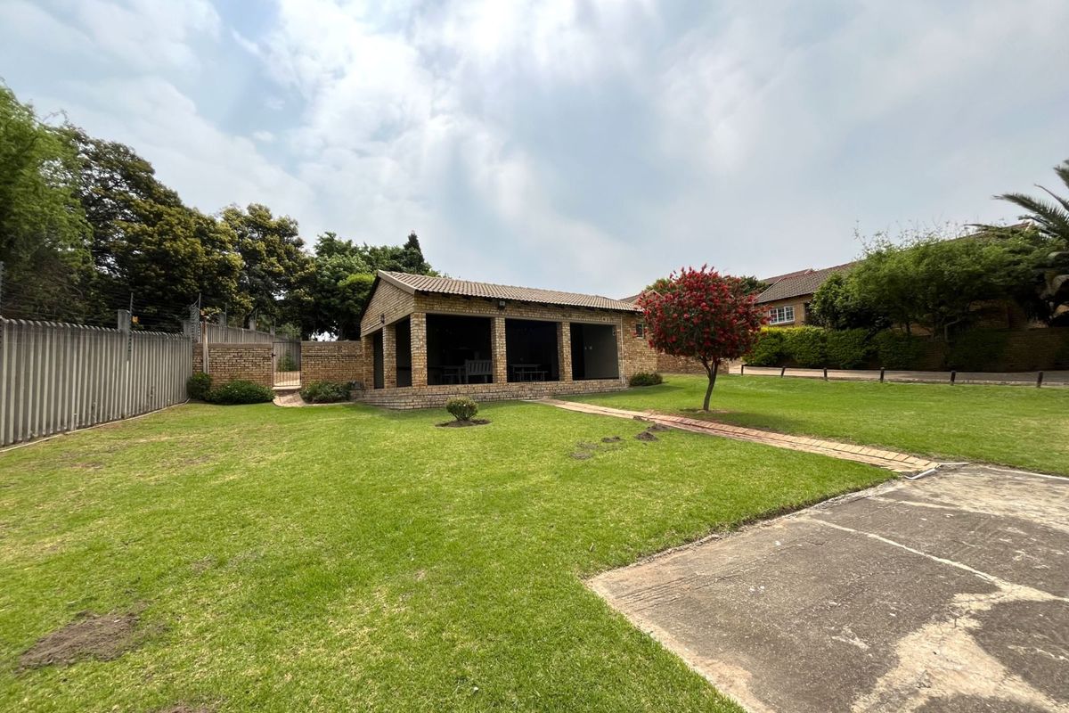 A spacious rear garden featuring a covered brick patio area, established lawn, and perimeter fencing.