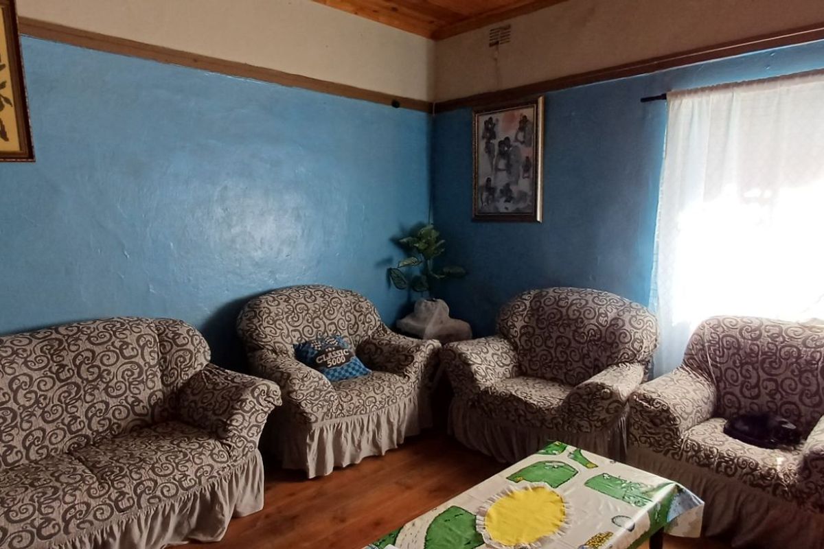 A living room featuring blue painted walls, timber ceiling, and wooden flooring, providing a dated but functional space.