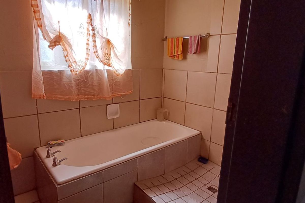 A functional bathroom featuring a built-in bathtub with tiled surround, wall-mounted towel rail, and a window providing natural light.
