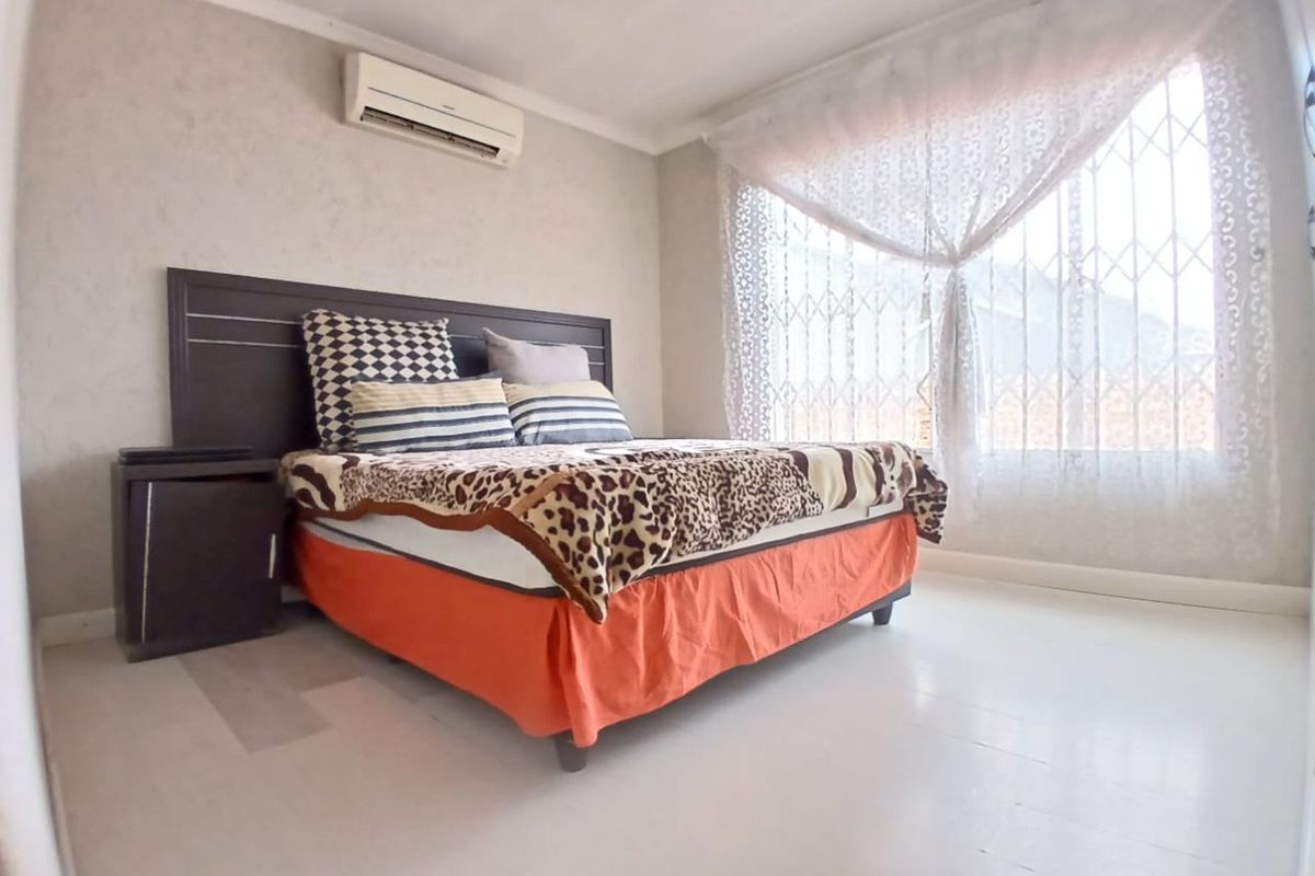 A bedroom featuring a wall-mounted air conditioning unit and security gate on the window, providing a functional and secure living space.
