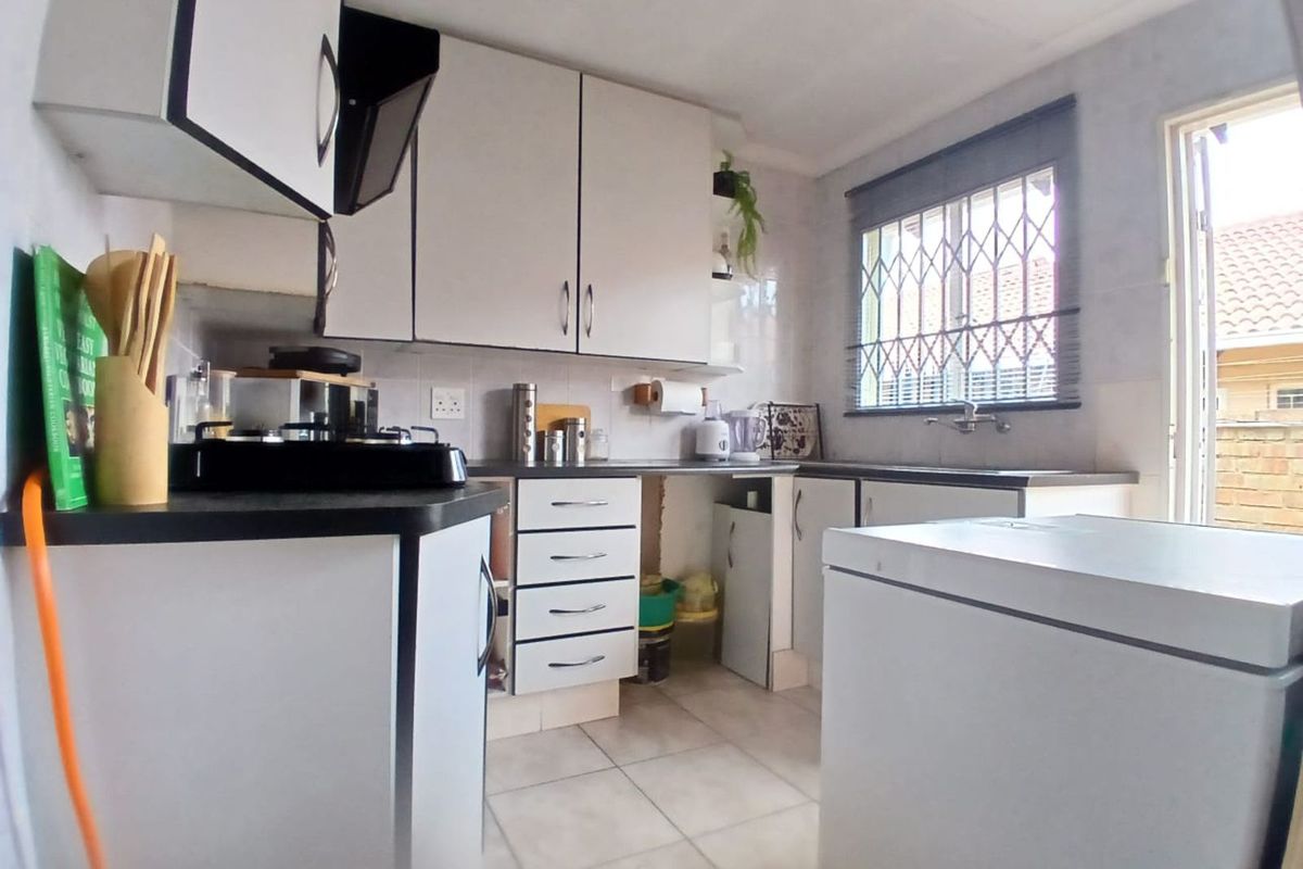 Functional kitchen featuring white cabinetry, dark countertops, tiled flooring, and a window with security bars, providing direct access to the exterior.
