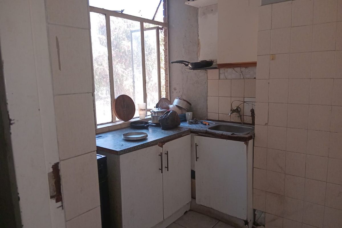 A dated kitchen area featuring basic cabinetry, a single sink, and tiled walls, requiring significant renovation and modernization.