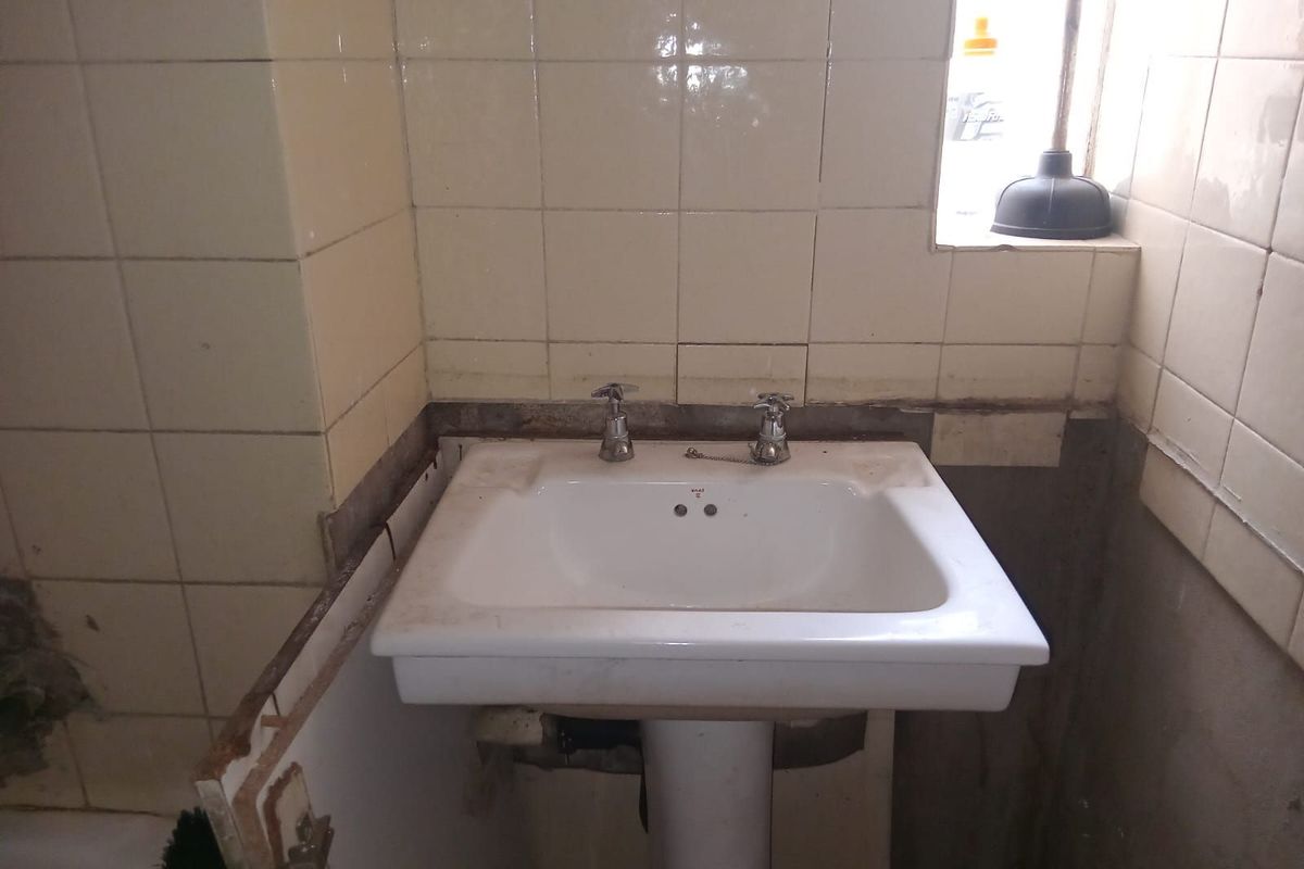 A bathroom vanity area featuring a pedestal sink with exposed wall sections and missing tile work, requiring renovation and repair.