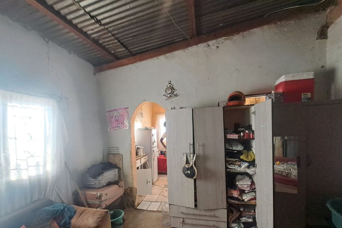 A bedroom space featuring exposed corrugated metal roofing, arched doorway access, and basic wall finishes requiring maintenance and renovation.