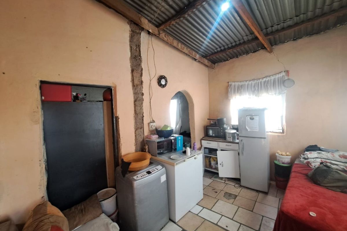 A basic kitchen area featuring exposed corrugated iron roofing, tiled flooring, and simple cabinetry, requiring significant renovation and structural repairs.